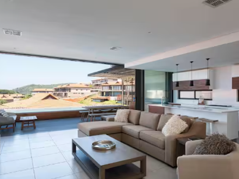 Modern open-plan living area featuring a sleek kitchen with island, seamless indoor-outdoor flow through large sliding doors, and expansive views.
