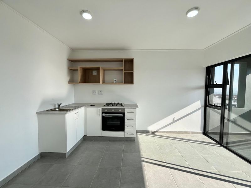 Modern, minimalist kitchen featuring white cabinetry, built-in oven, gas hob, stainless steel sink, and open shelving, set against neutral tiled flooring.