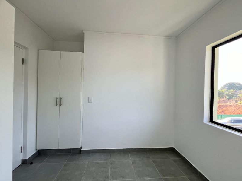 A clean, empty bedroom featuring neutral tiled flooring, a built-in wardrobe, and a window with natural light.