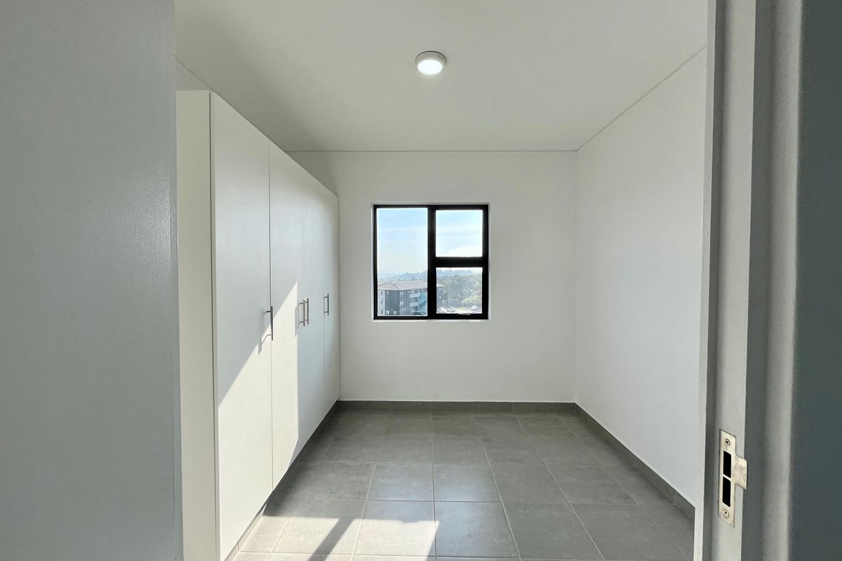 A bright, empty bedroom featuring neutral tiled flooring, built-in white cupboards, and a window with natural light.