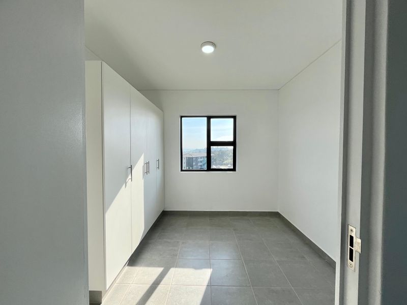 A bright, empty bedroom featuring neutral tiled flooring, built-in white cupboards, and a window with natural light.