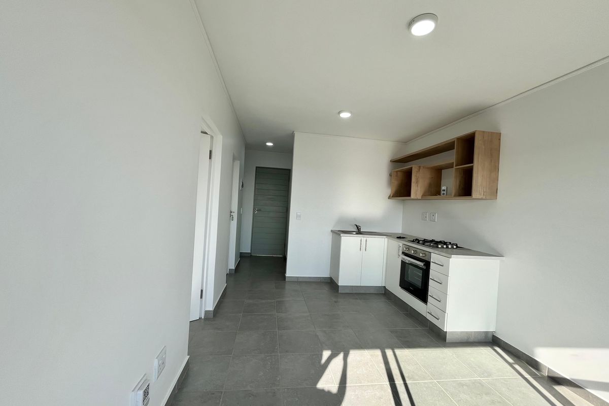 Modern, minimalist kitchen featuring white cabinetry, built-in oven, gas hob, and open shelving, set against neutral tiled flooring in an open-plan layout.