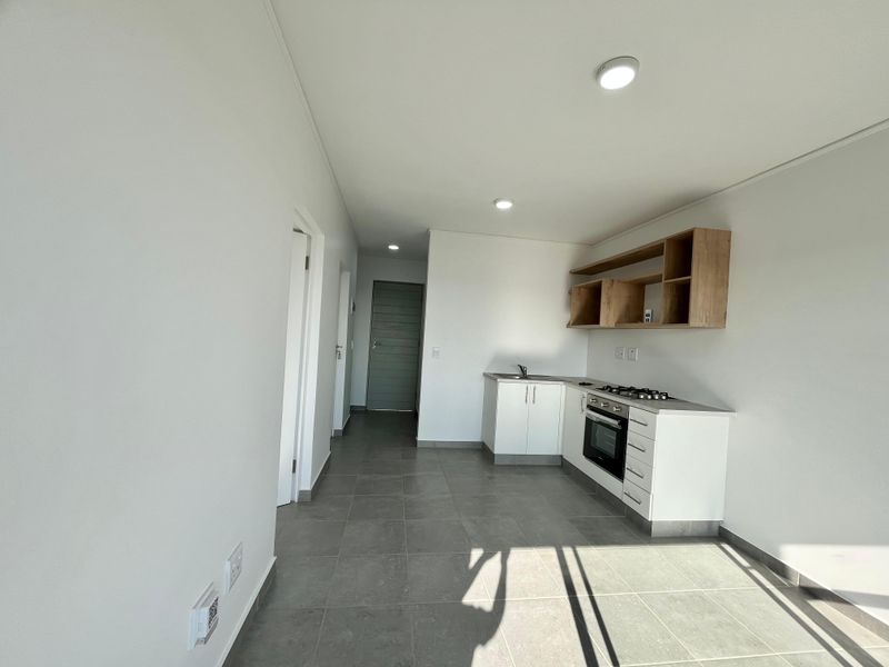 Modern, minimalist kitchen featuring white cabinetry, built-in oven, gas hob, and open shelving, set against neutral tiled flooring in an open-plan layout.