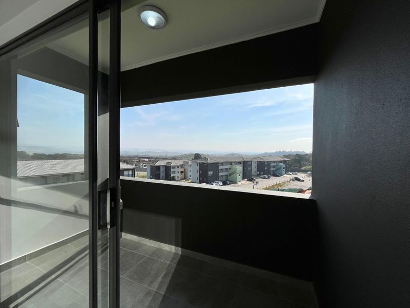 A modern covered balcony featuring tiled flooring, a sliding glass door, and an open view of the surrounding apartment complex.