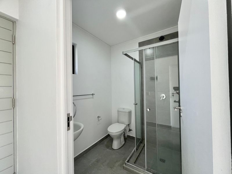 A clean, modern bathroom featuring a glass-enclosed shower, a wall-mounted basin, and neutral grey floor tiles.