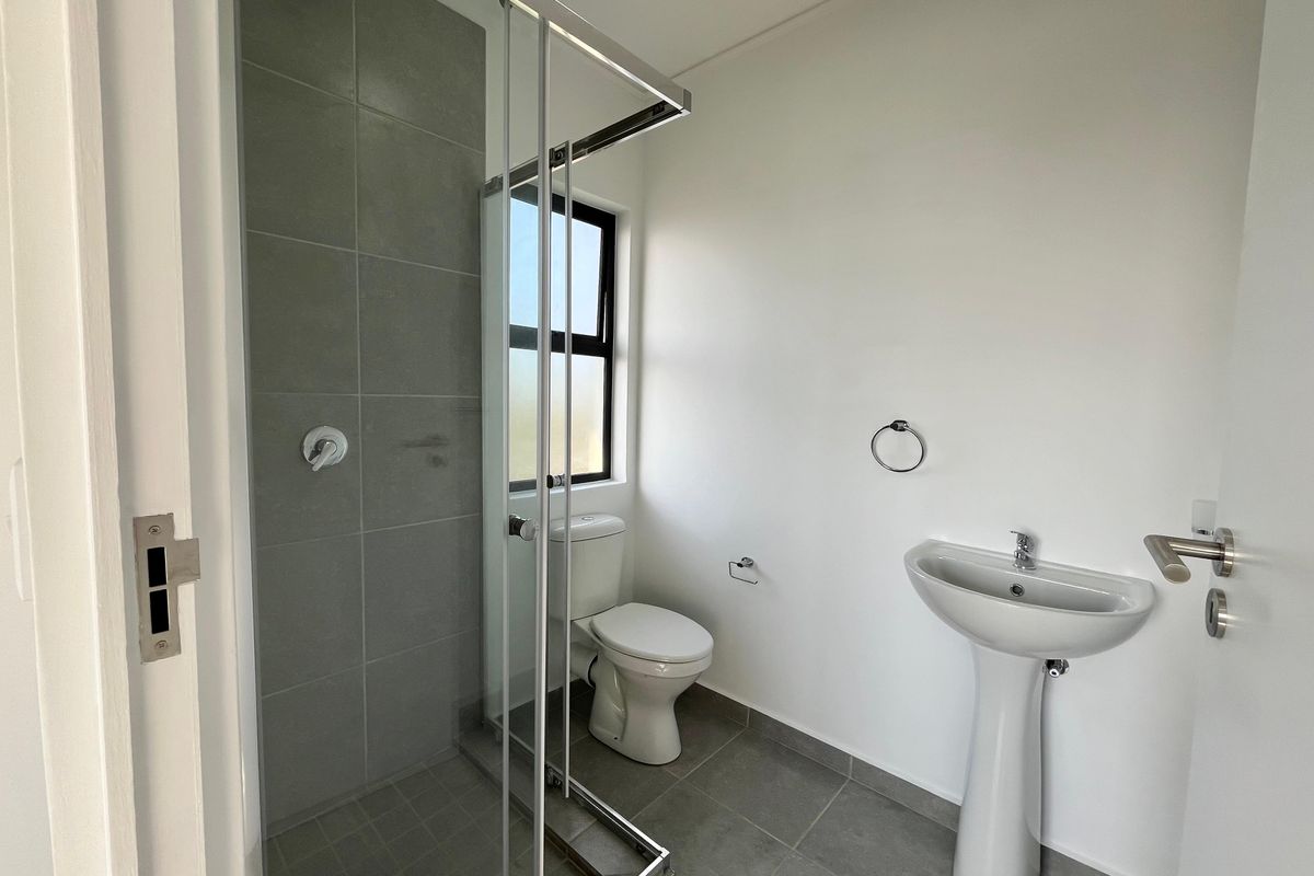 A clean, modern bathroom featuring a pedestal basin, toilet, and a glass-enclosed shower with grey floor and wall tiling.