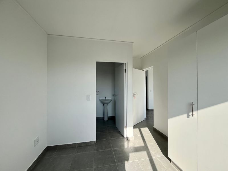 A bright, empty hallway featuring tiled flooring, built-in cupboards, and access to an adjacent bathroom with a pedestal basin.