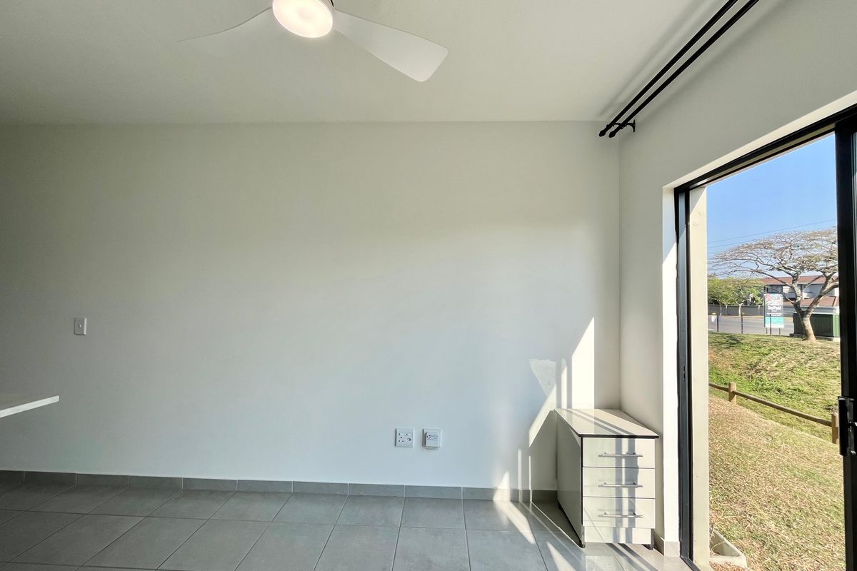 A bright, empty bedroom featuring tiled flooring, a modern ceiling fan, and a sliding glass door providing access to the exterior.