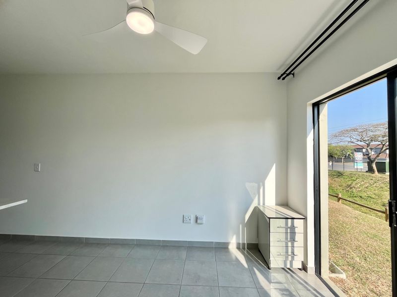 A bright, empty bedroom featuring tiled flooring, a modern ceiling fan, and a sliding glass door providing access to the exterior.