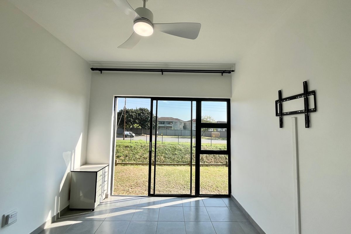 A bright, empty living room featuring tiled floors, a modern ceiling fan, and a large sliding glass door leading to the exterior.