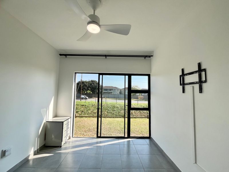 A bright, empty living room featuring tiled floors, a modern ceiling fan, and a large sliding glass door leading to the exterior.