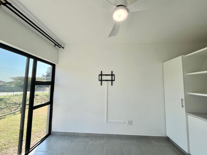 A bright, empty bedroom featuring tiled floors, built-in storage cabinetry, a ceiling fan, and large windows with views of the exterior.