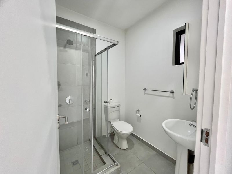 A clean and functional bathroom featuring a glass-enclosed shower, pedestal sink, and toilet with neutral tiled flooring.