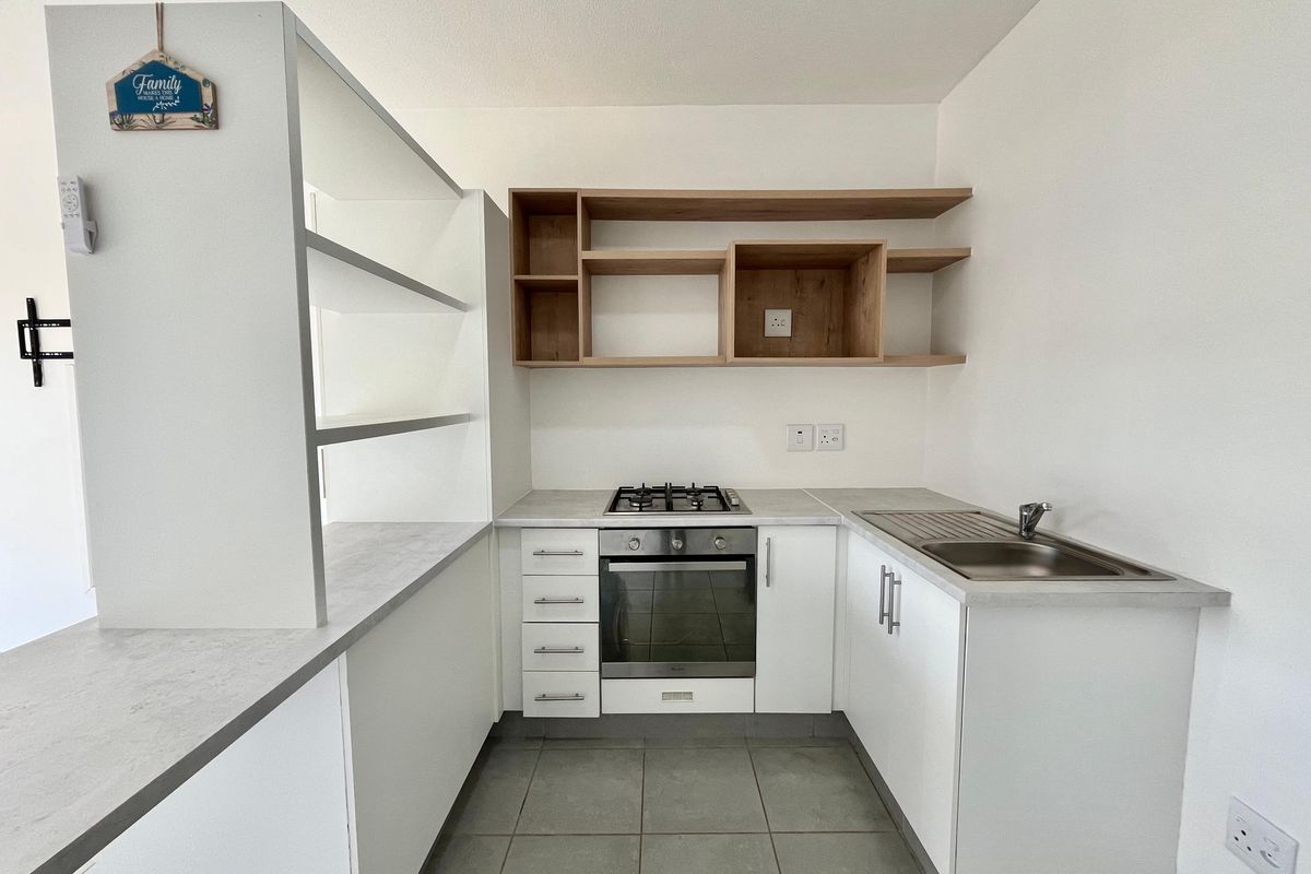 A clean, modern kitchen featuring built-in cabinetry, a gas hob, an oven, stainless steel sink, and open wooden shelving.