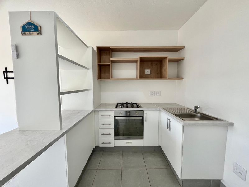 A clean, modern kitchen featuring built-in cabinetry, a gas hob, an oven, stainless steel sink, and open wooden shelving.