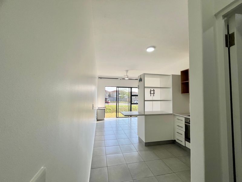 An open-plan living and kitchen area featuring tiled flooring, built-in cabinetry, a breakfast counter, and a sliding glass door leading to the exterior.