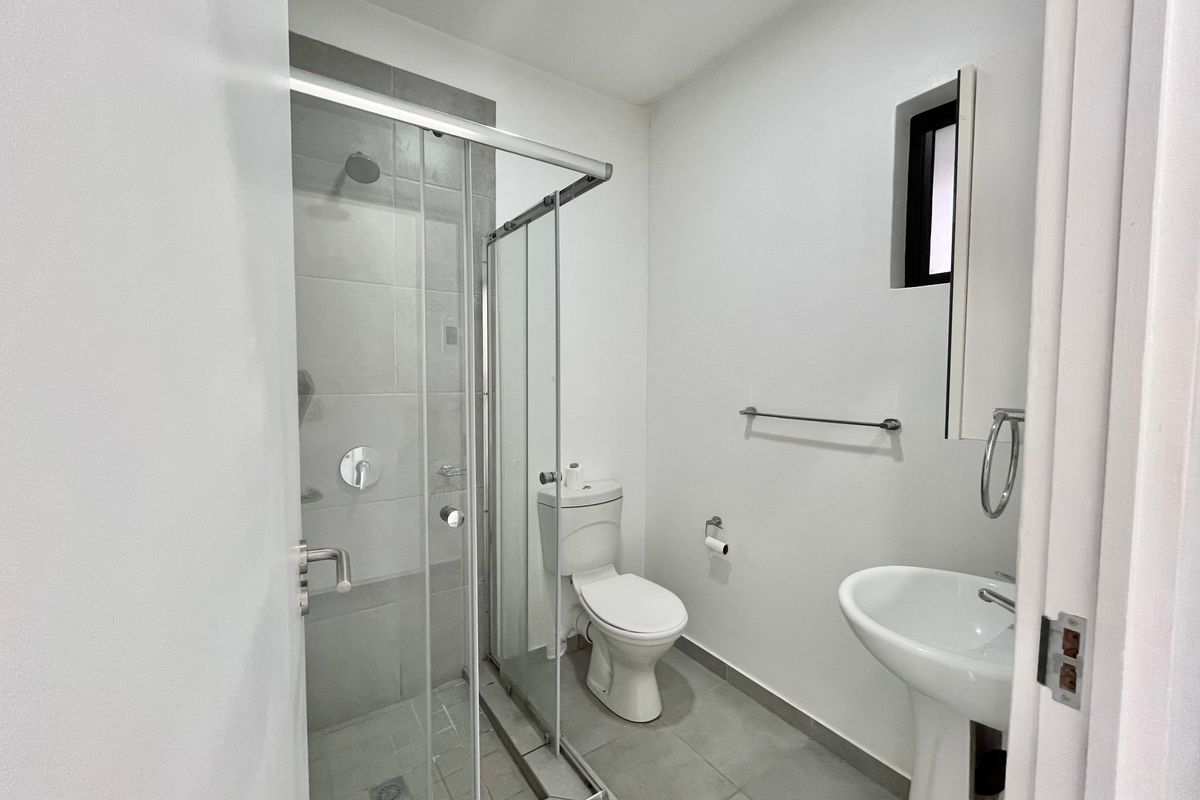 A clean and functional bathroom featuring a glass-enclosed shower, pedestal sink, and toilet with neutral tiled flooring.