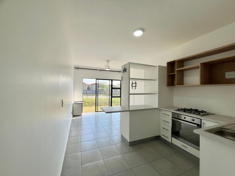 Modern open-plan kitchen and living area featuring tiled floors, built-in cabinetry, gas hob, oven, and direct access to the exterior through sliding glass doors.