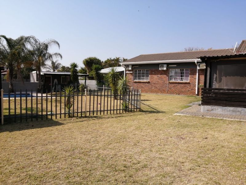 Rear view of the property featuring a brick facade, tiled roof, security bars, and a spacious garden with a swimming pool and paved patio area.
