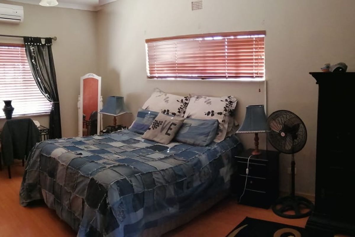 A bedroom featuring laminate flooring, timber venetian blinds, and a wall-mounted split-system air conditioning unit.