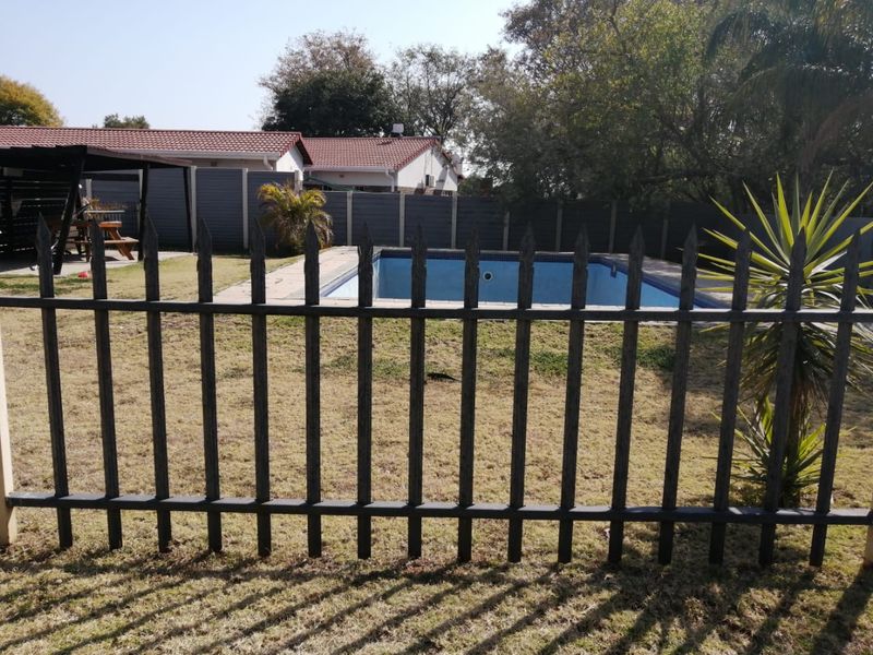 Outdoor pool area featuring a paved surround, metal perimeter fencing, and a covered patio structure in the rear garden.