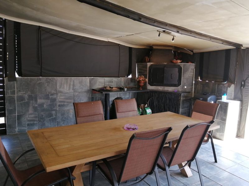 Covered patio area featuring a built-in braai, stone wall cladding, and durable tiled flooring, suitable for outdoor dining and entertainment.