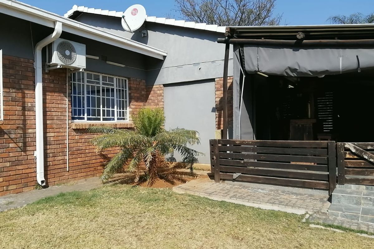 Rear exterior view of the house featuring a brick facade, covered patio area with timber decking, and a small garden space.