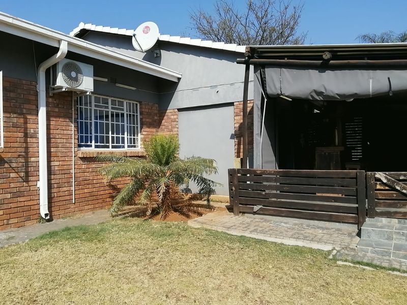 Rear exterior view of the house featuring a brick facade, covered patio area with timber decking, and a small garden space.