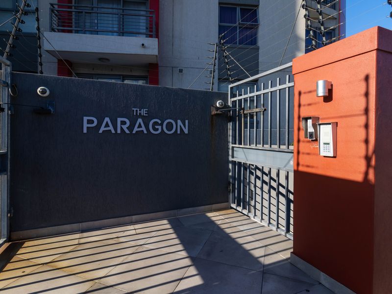 Secure entrance to The Paragon apartment complex featuring a gated access point, intercom system, and perimeter electric fencing.