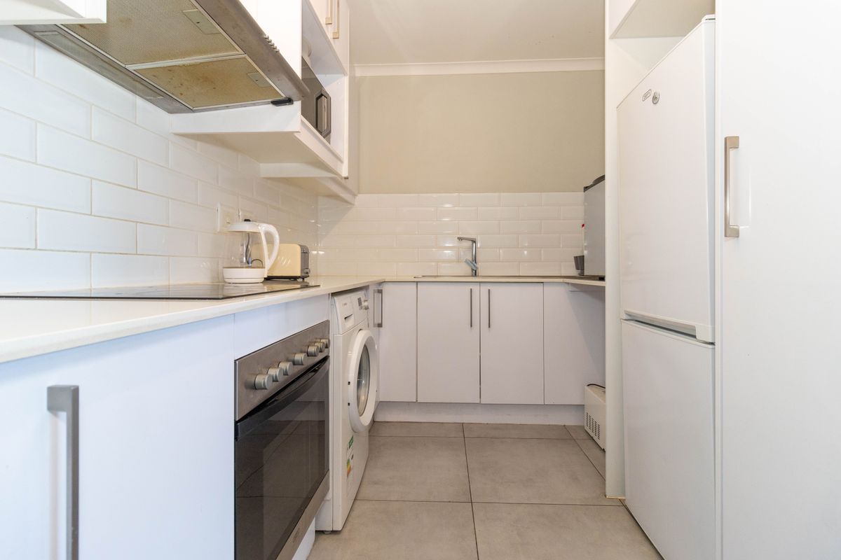 Compact kitchen featuring white cabinetry, subway tile backsplash, built-in oven, electric hob, and integrated laundry plumbing.