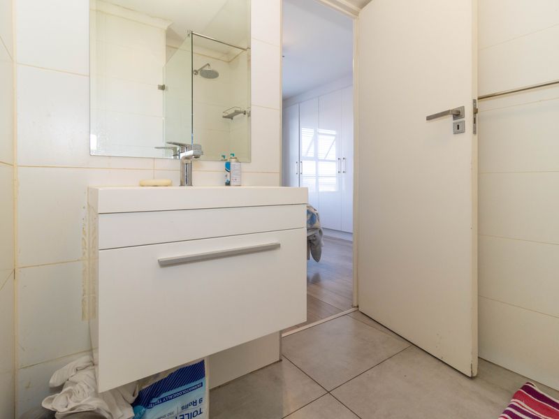 A functional bathroom featuring a modern vanity cabinet, basin, and a glass-enclosed shower area with tiled finishes.