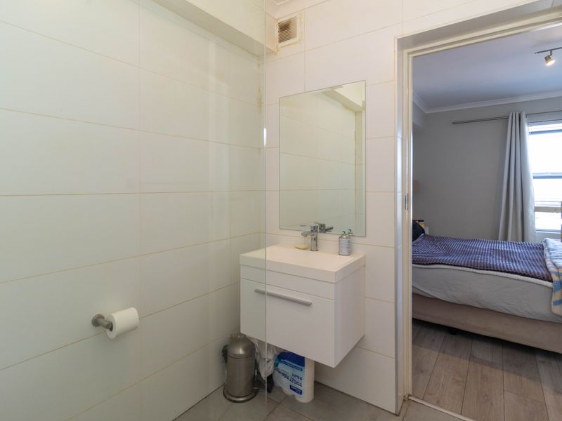 Compact bathroom featuring a wall-mounted vanity, basin, and glass shower screen, with direct access to the adjacent bedroom.