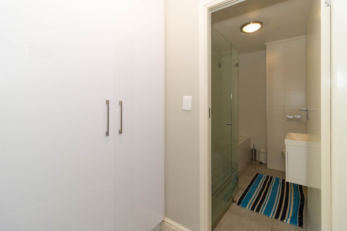 A clean bathroom featuring a glass-enclosed shower, wall-mounted vanity, and a built-in storage cupboard in the adjacent hallway area.