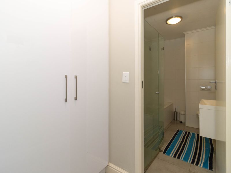 A clean bathroom featuring a glass-enclosed shower, wall-mounted vanity, and a built-in storage cupboard in the adjacent hallway area.