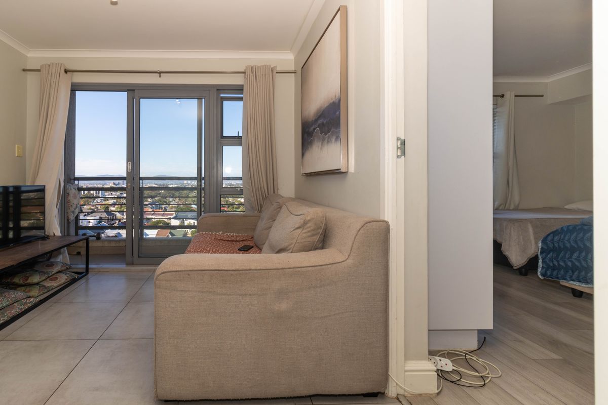 A bright living room featuring tiled flooring and a sliding glass door leading to a balcony with expansive city views.