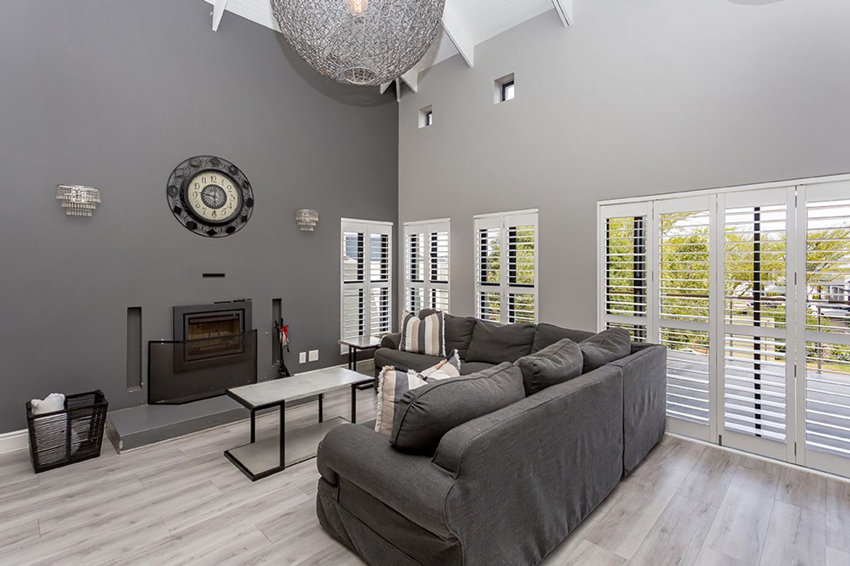 Spacious living room featuring a vaulted ceiling, a built-in fireplace, modern laminate flooring, and plantation shutters providing ample natural light.