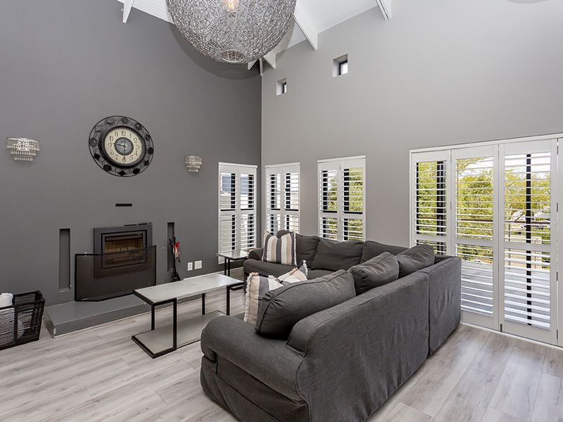 Spacious living room featuring a vaulted ceiling, a built-in fireplace, modern laminate flooring, and plantation shutters providing ample natural light.
