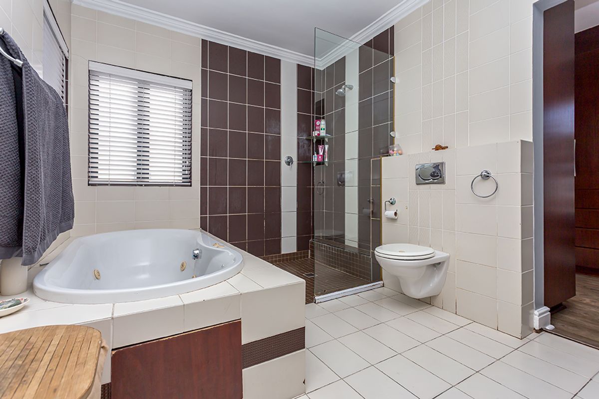 A functional bathroom featuring a built-in corner bathtub, a separate glass-enclosed shower, and a wall-mounted toilet with neutral tiled finishes.
