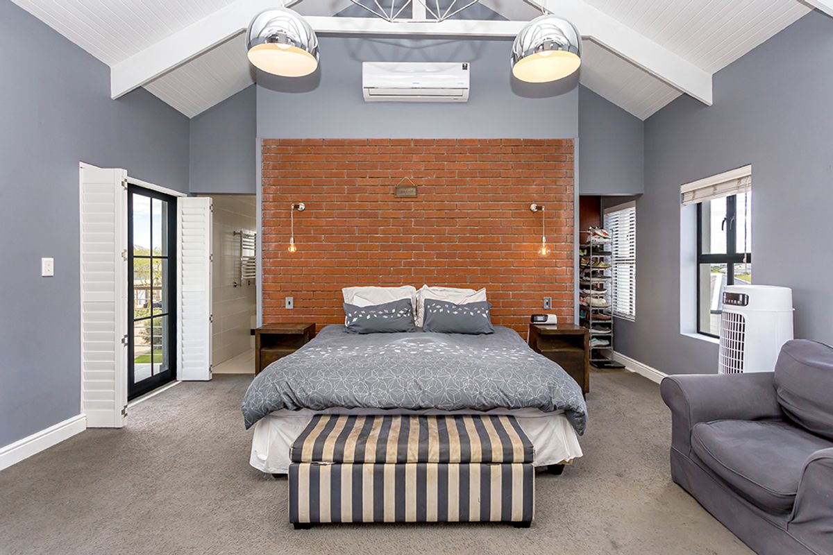 Spacious bedroom featuring a vaulted ceiling, exposed brick feature wall, split-system air conditioning, and direct access to an en-suite bathroom.