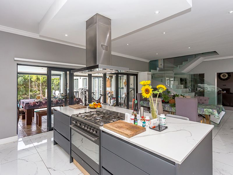 Modern open-plan kitchen featuring a large island with gas cooktop, stone countertops, and seamless flow to the outdoor patio and staircase area.