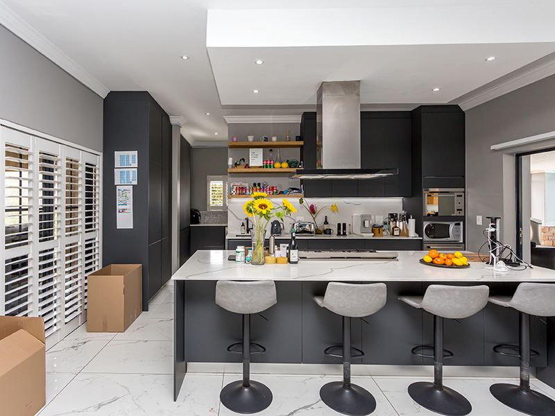 Modern kitchen featuring a large central island with stone countertops, dark cabinetry, integrated appliances, and sleek tiled flooring with plantation shutters.