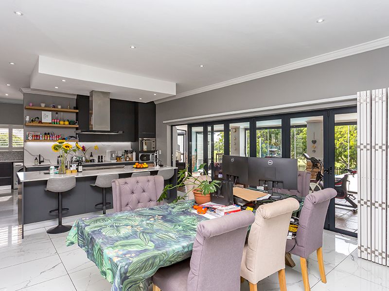 Modern open-plan kitchen and dining area featuring a large island, sleek cabinetry, marble-look flooring, and expansive bi-fold doors leading to the outdoor space.