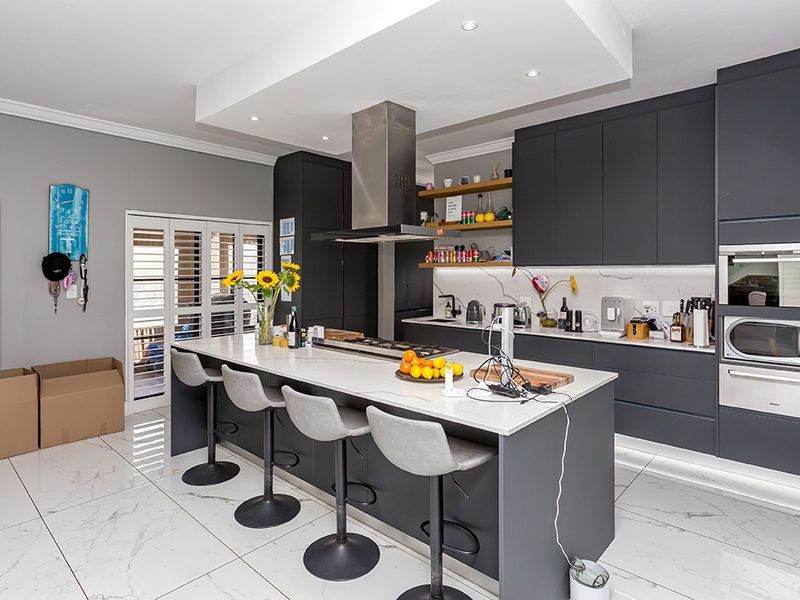 Modern kitchen featuring dark cabinetry, a large central island with stone countertops, built-in appliances, and elegant marble-look floor tiles.