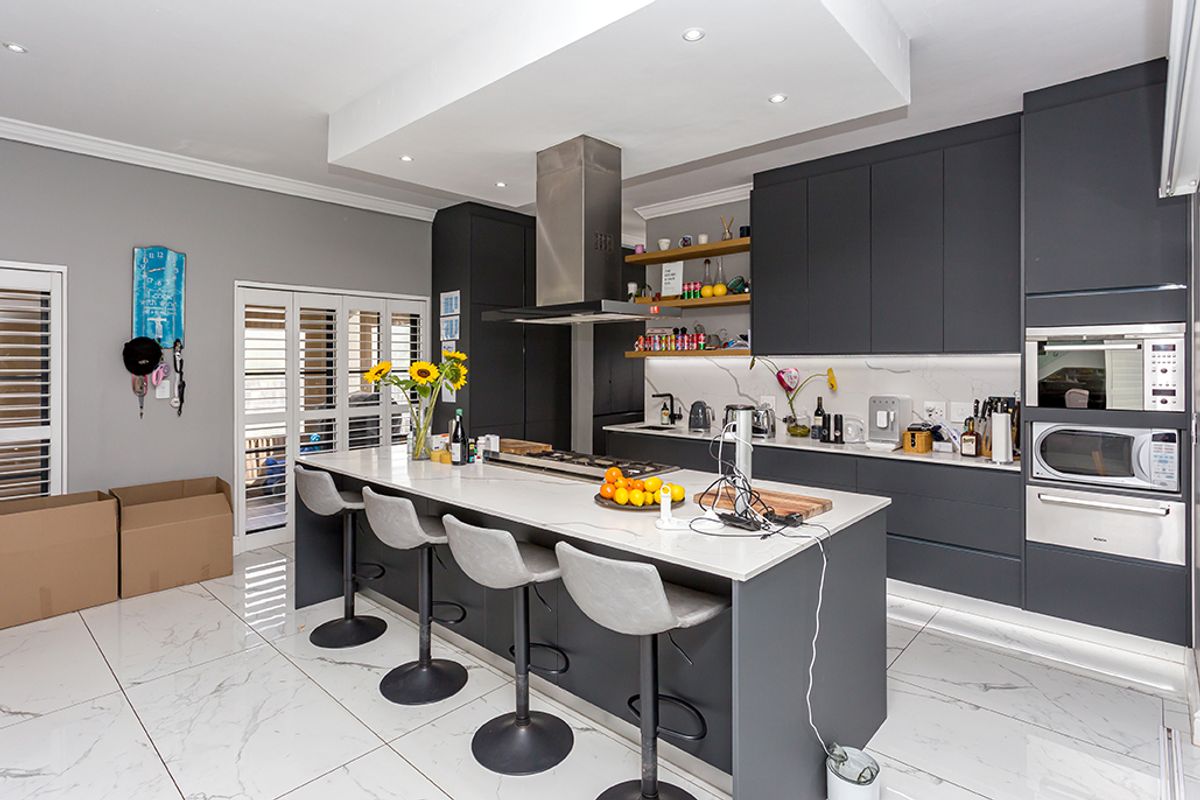 Modern kitchen featuring dark cabinetry, a large central island with stone countertops, built-in appliances, and elegant marble-look floor tiles.