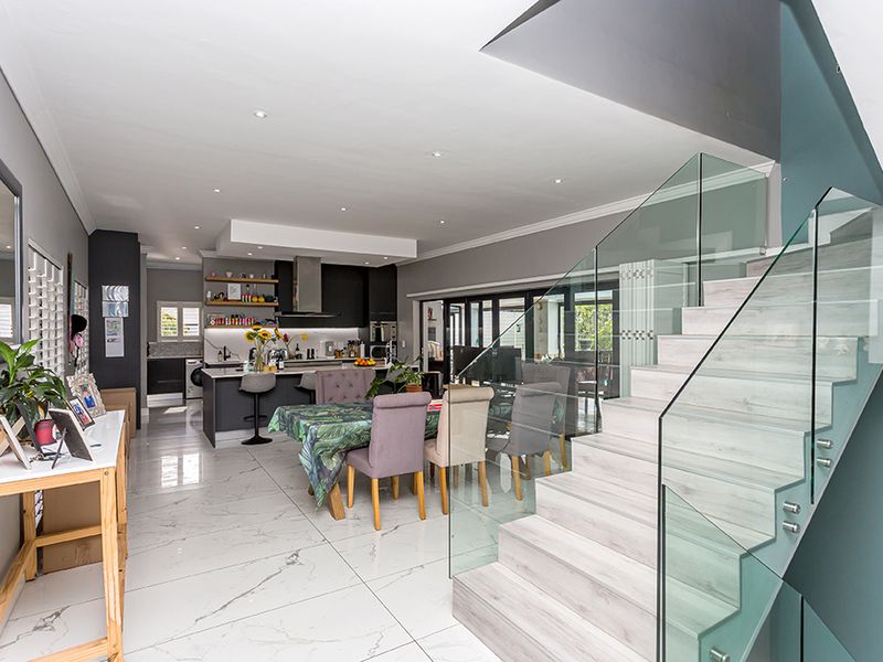 Modern open-plan living area featuring high-gloss marble-look flooring, a contemporary staircase with glass balustrades, and a sleek kitchen with a central island.