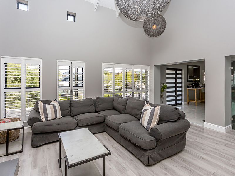 Spacious living room featuring high vaulted ceilings, modern laminate flooring, and plantation shutters, creating a bright and airy atmosphere.