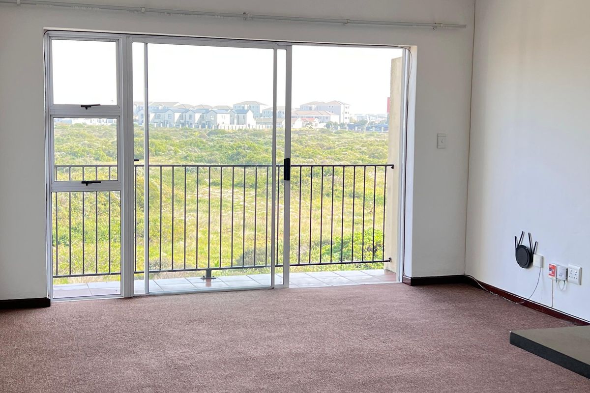 An empty living room featuring carpeted flooring and a large sliding glass door that opens onto a balcony with scenic views.
