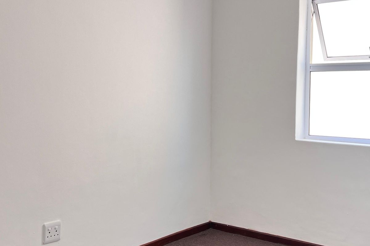 An empty bedroom featuring neutral walls, carpeted flooring, and a window, providing a blank canvas for personalization.