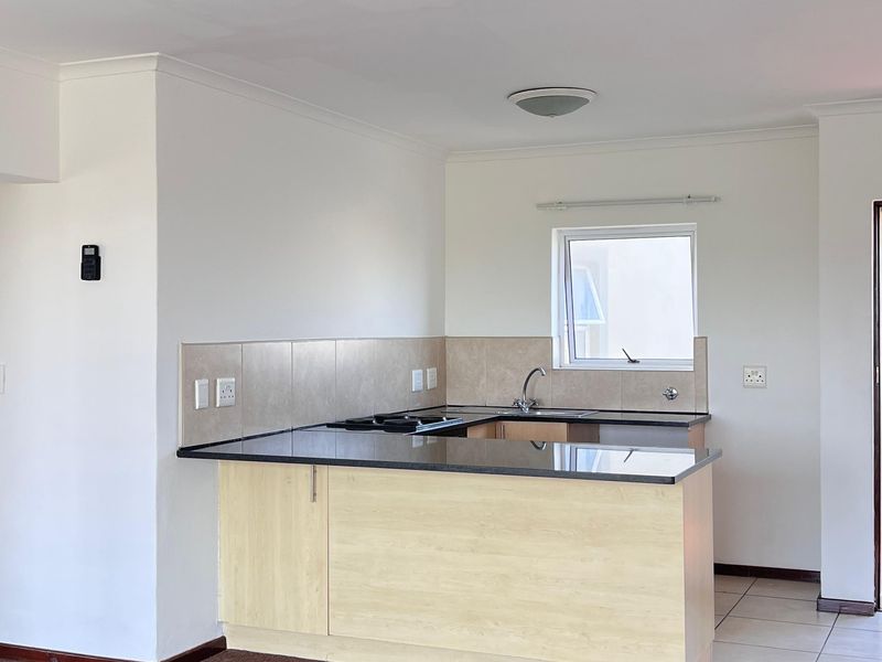 Open-plan kitchen and living area featuring light wood cabinetry, dark countertops, tiled kitchen flooring, and carpeted living space.