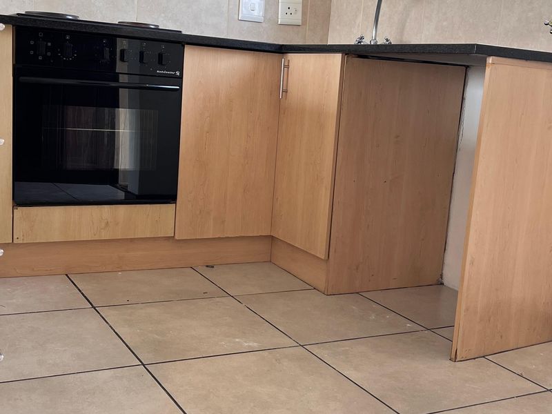 A compact kitchen featuring light wood-finish cabinetry, a built-in oven, hob, and tiled splashback, currently requiring minor repairs to cabinetry.